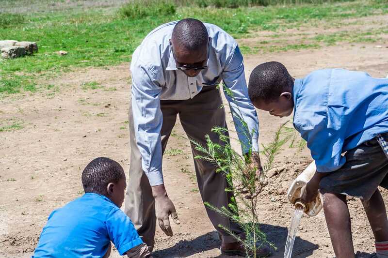 Kenyan man showing two school children how to plant trees